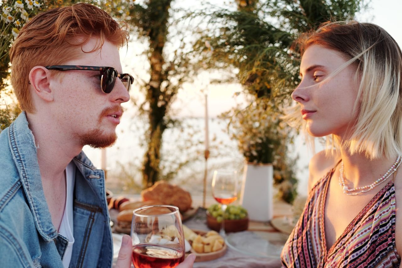 Couple enjoys wine and conversation during a beachside date at sunset.